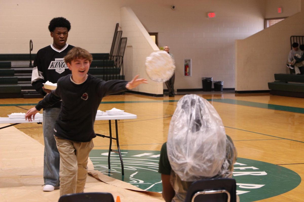 A pie, hurled towards Joe Hughes by Drake Arnold, is caught gracefully soaring through the air, observed by Gabriel Peters.